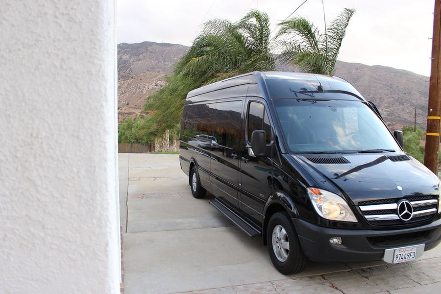 Black Mercedes-Benz Sprinter van, ideal for rv rental, parked on a driveway with mountains and palm trees behind it.