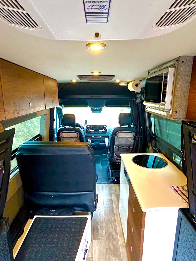 An RV rental's functional interior: looking forward past a kitchen counter, microwave, & storage towards the front cabin seats. — photo 14