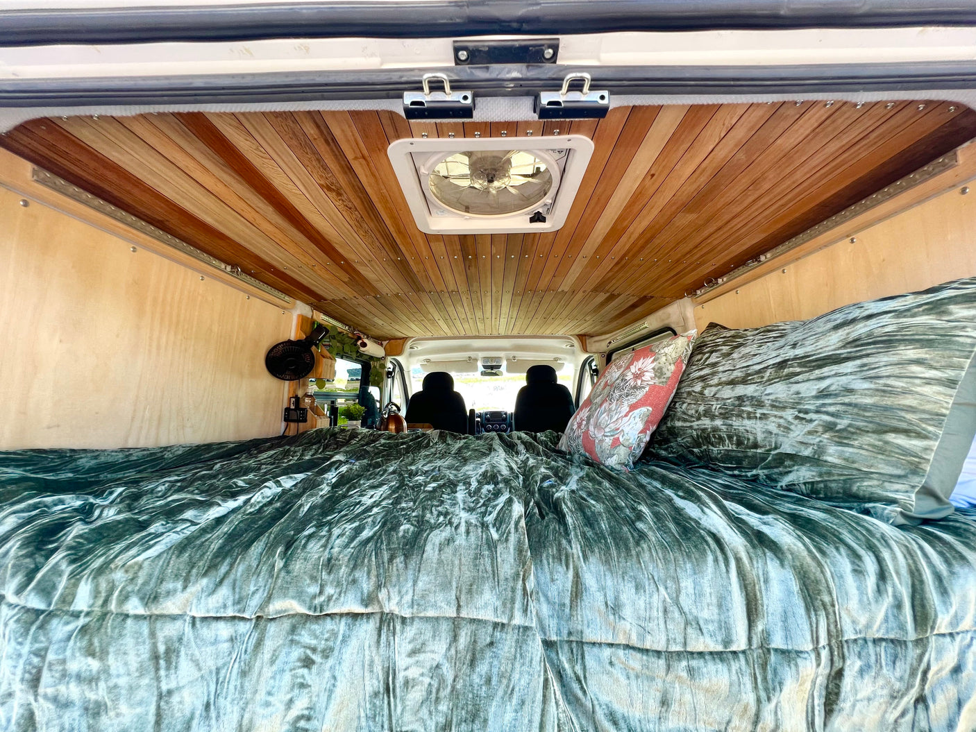 Cozy RV rental interior with a plush bed, wooden ceiling, and fan, offering a view towards the front cabin.
