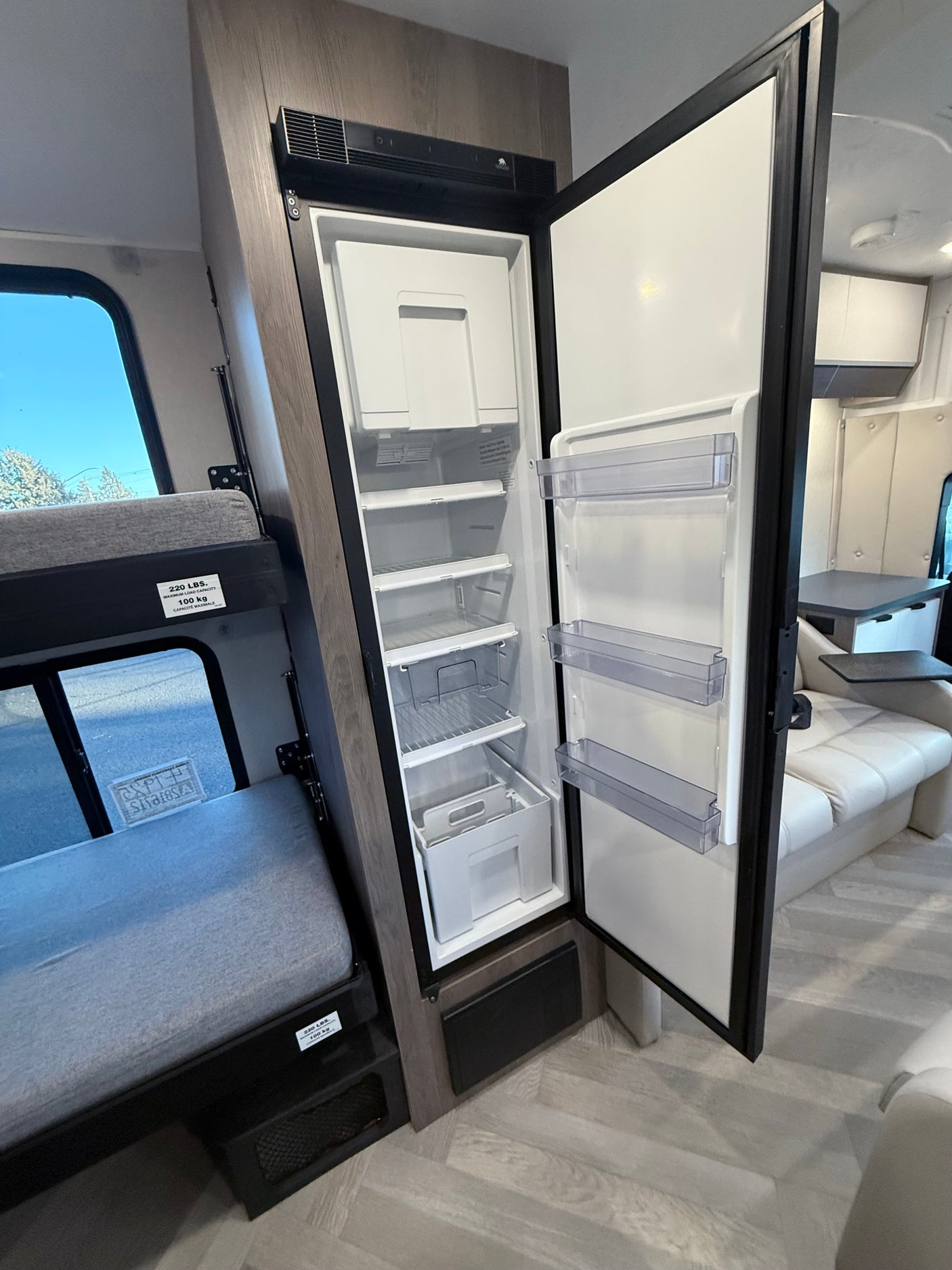 Inside an RV rental: a full-size refrigerator with freezer, a 220 lbs capacity bunk bed, and a comfortable lounge area.