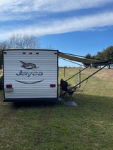 RV rental: Jayco travel trailer in a grassy field, with its awning extended and outdoor seating for relaxation.