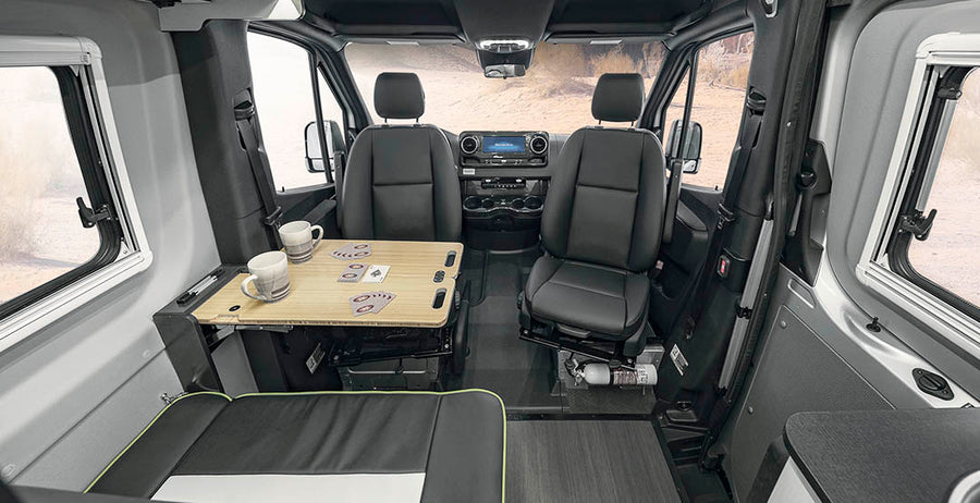 Inside an RV rental, showing swivel seats, a table for games/dining, and a compact, functional living area.