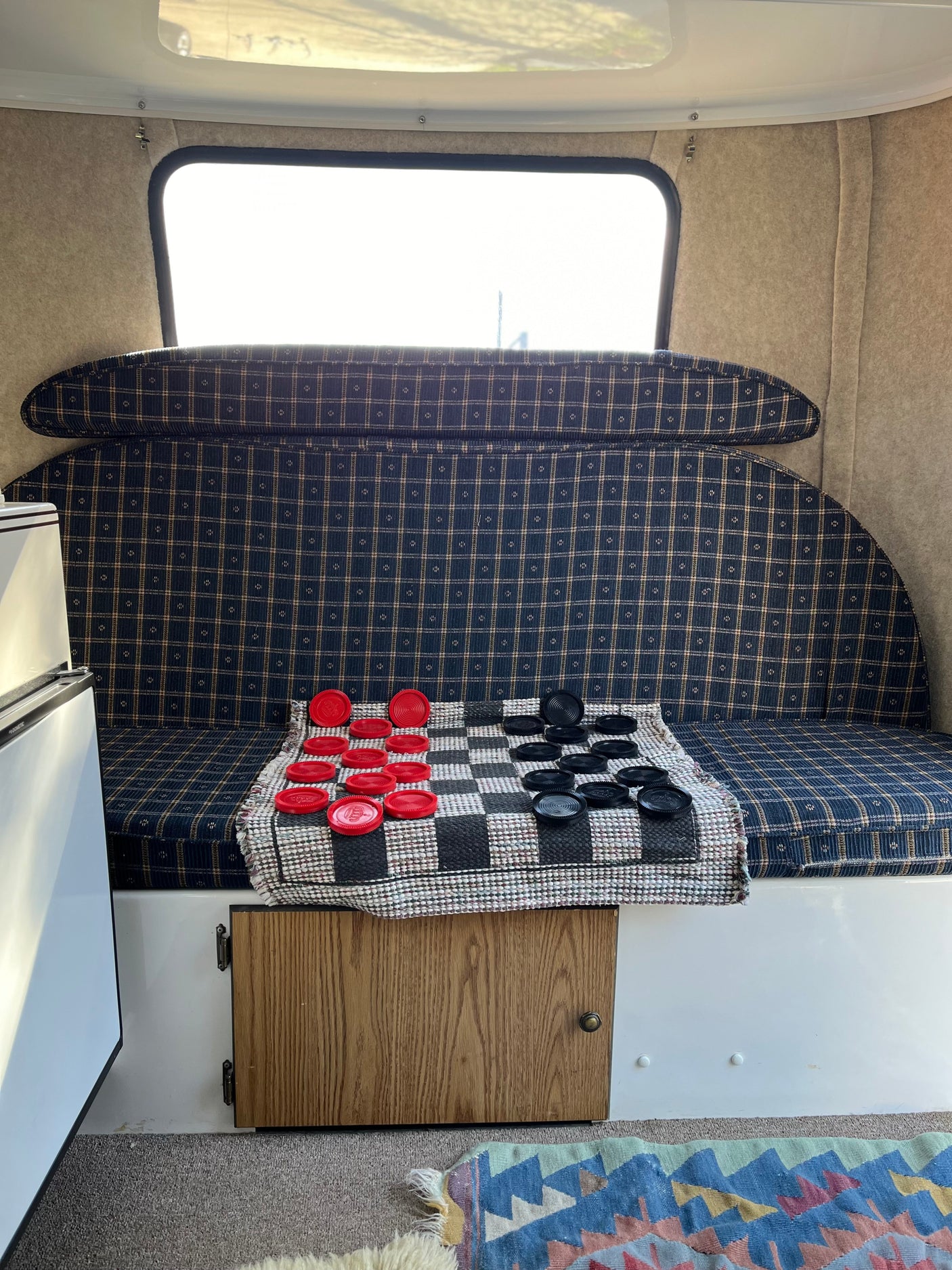 Inside a cozy rv rental: plaid seating, bright window, and a checkers game laid out on a mat.