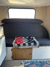 Inside a cozy rv rental: plaid seating, bright window, and a checkers game laid out on a mat.