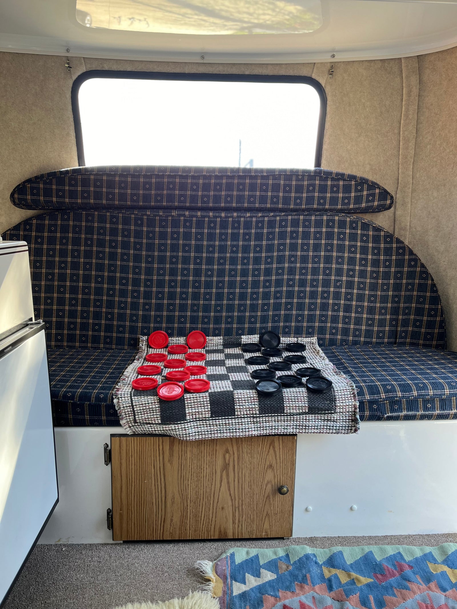 Inside a cozy rv rental: plaid seating, bright window, and a checkers game laid out on a mat.
