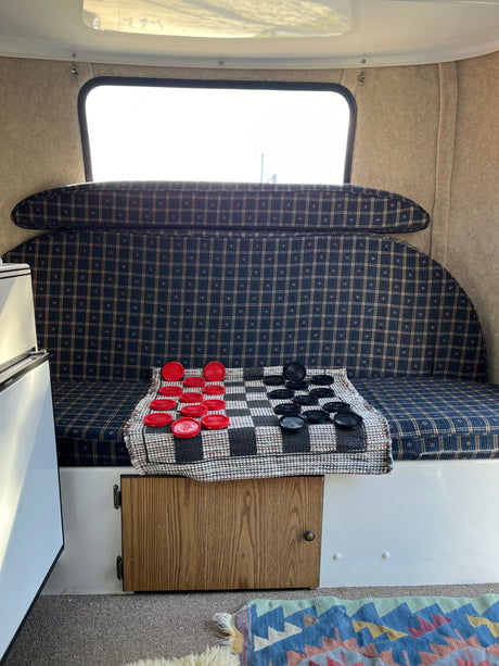 Inside a cozy rv rental: plaid seating, bright window, and a checkers game laid out on a mat.