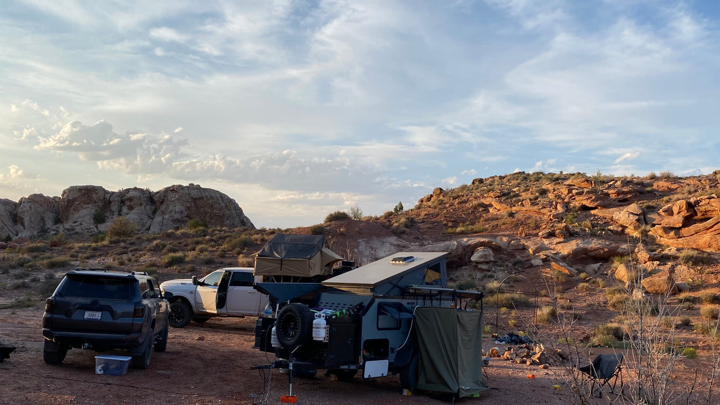 Off-road desert camping setup featuring an expedition trailer, SUV, and truck. Consider this RV rental for adventure.