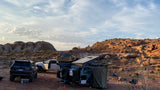 Off-road desert camping setup featuring an expedition trailer, SUV, and truck. Consider this RV rental for adventure.