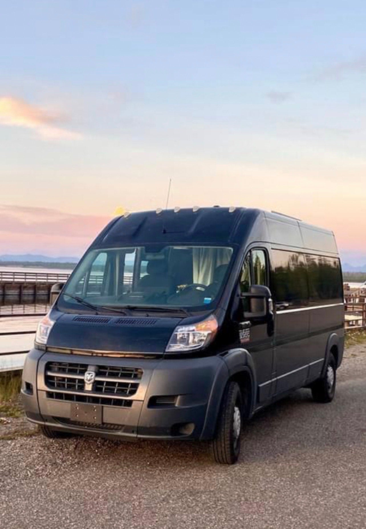 This spacious black camper van, ideal for RV rental adventures, is parked on gravel overlooking a scenic lake at sunset. — photo 2