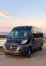 This spacious black camper van, ideal for RV rental adventures, is parked on gravel overlooking a scenic lake at sunset.