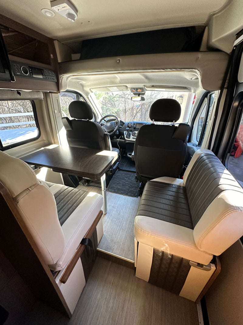 Spacious RV rental interior: dinette with two-tone seating, adjustable table, and view to driver's cabin. — photo 4