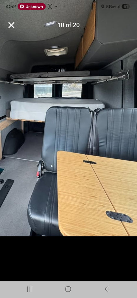 RV rental: Camper van interior with a lower bed, upper bunk, two black seats, and a bamboo folding table.