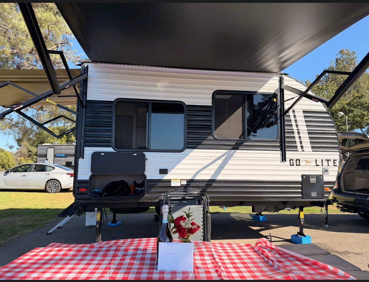 Go Lite RV rental ready for a romantic camping trip with a picnic table, champagne, and roses under extended awnings.