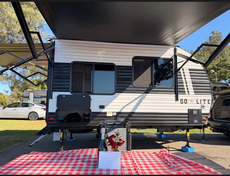 Go Lite RV rental ready for a romantic camping trip with a picnic table, champagne, and roses under extended awnings.
