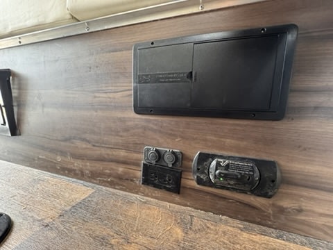 RV rental interior: electrical panel, 12V outlets, and CO detector mounted on a wood-grain wall for safety and power.