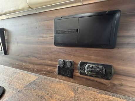 RV rental interior: electrical panel, 12V outlets, and CO detector mounted on a wood-grain wall for safety and power.