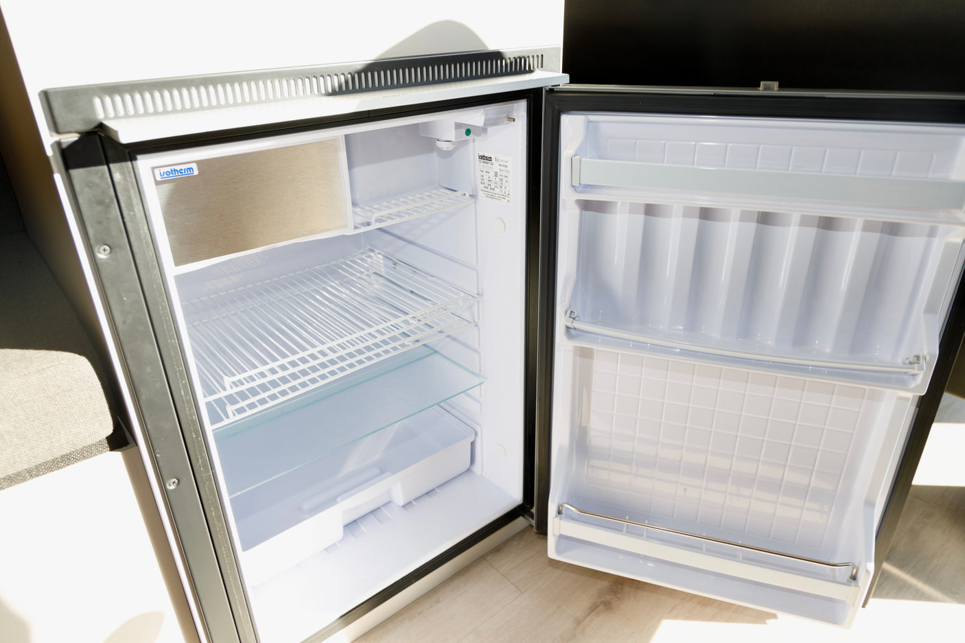 An open Isotherm compact refrigerator inside an RV rental. View of empty shelves, door bins, and small freezer.