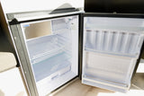 An open Isotherm compact refrigerator inside an RV rental. View of empty shelves, door bins, and small freezer.