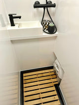 Modern RV rental wet bath, featuring a sleek black sink, shower, and discrete portable toilet on a wooden slatted floor.