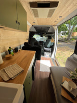 Inside a modern RV rental, showcasing a functional kitchen, cozy bed, and bright wooden interior.