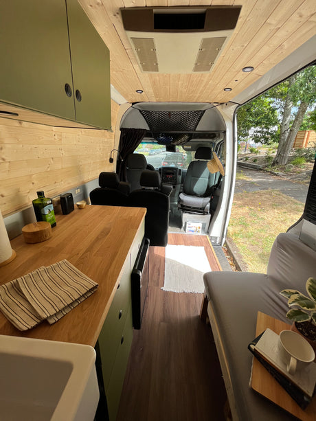 Inside a modern RV rental, showcasing a functional kitchen, cozy bed, and bright wooden interior.