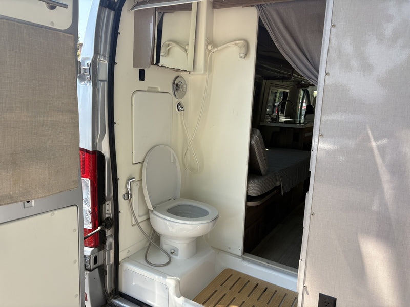 Inside an RV rental: a compact camper van bathroom with a toilet, shower, and mirror, seen from open doors. — photo 9