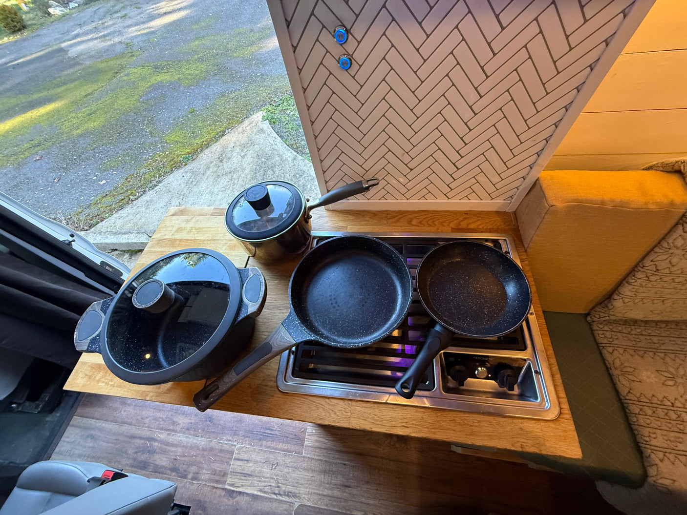 An RV rental kitchen shows a Dometic stovetop with pans & pot on a wood counter, blue accent lights, & herringbone backsplash.