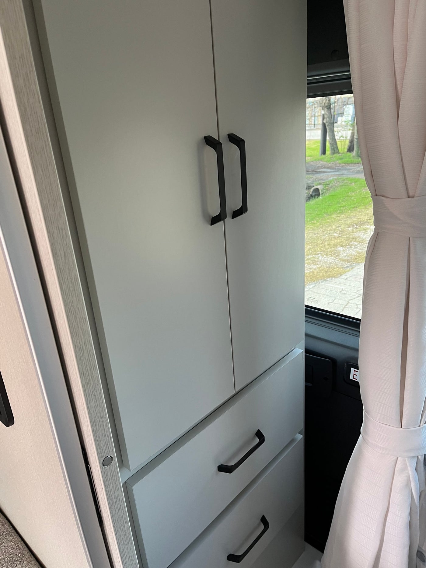 Modern RV rental interior features light grey cabinets, drawers, and a window with a tied-back curtain. — photo 17