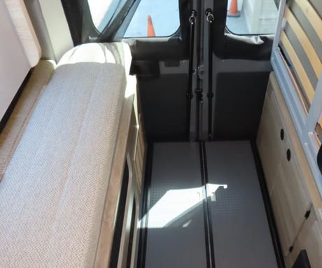 View inside an RV rental. Features a long fabric bench seat, central floor aisle, and slatted bed/storage area.