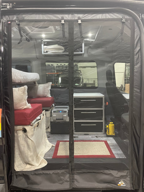 Inside an RV rental: a cozy, organized camper van interior with sleeping area, fridge, and storage, seen through a clear mesh screen.