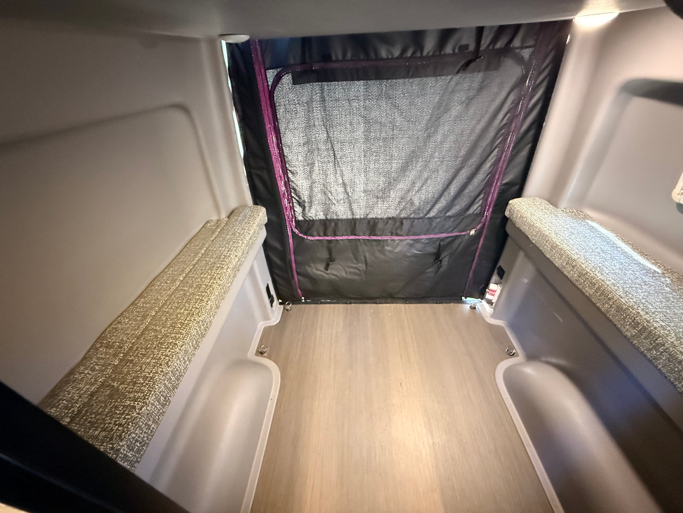 Interior of an RV rental: This compact space features cushioned benches, a wood-look floor, and a rear fabric door with mesh.