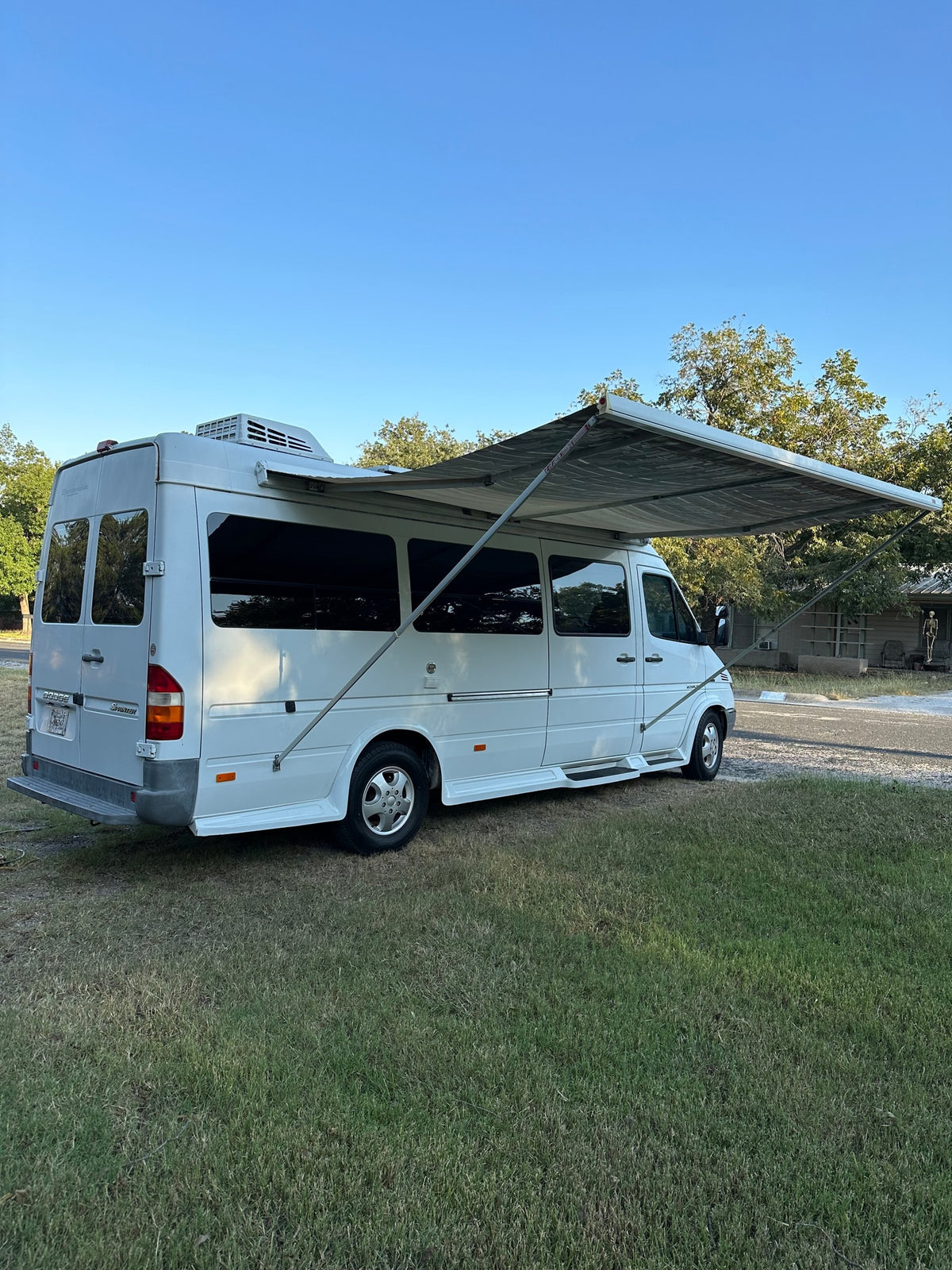 White Dodge Sprinter camper van with extended awning on grass