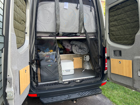 RV rental ready for adventure! Rear van view shows organized storage, bed, portable toilet & outdoor shower.