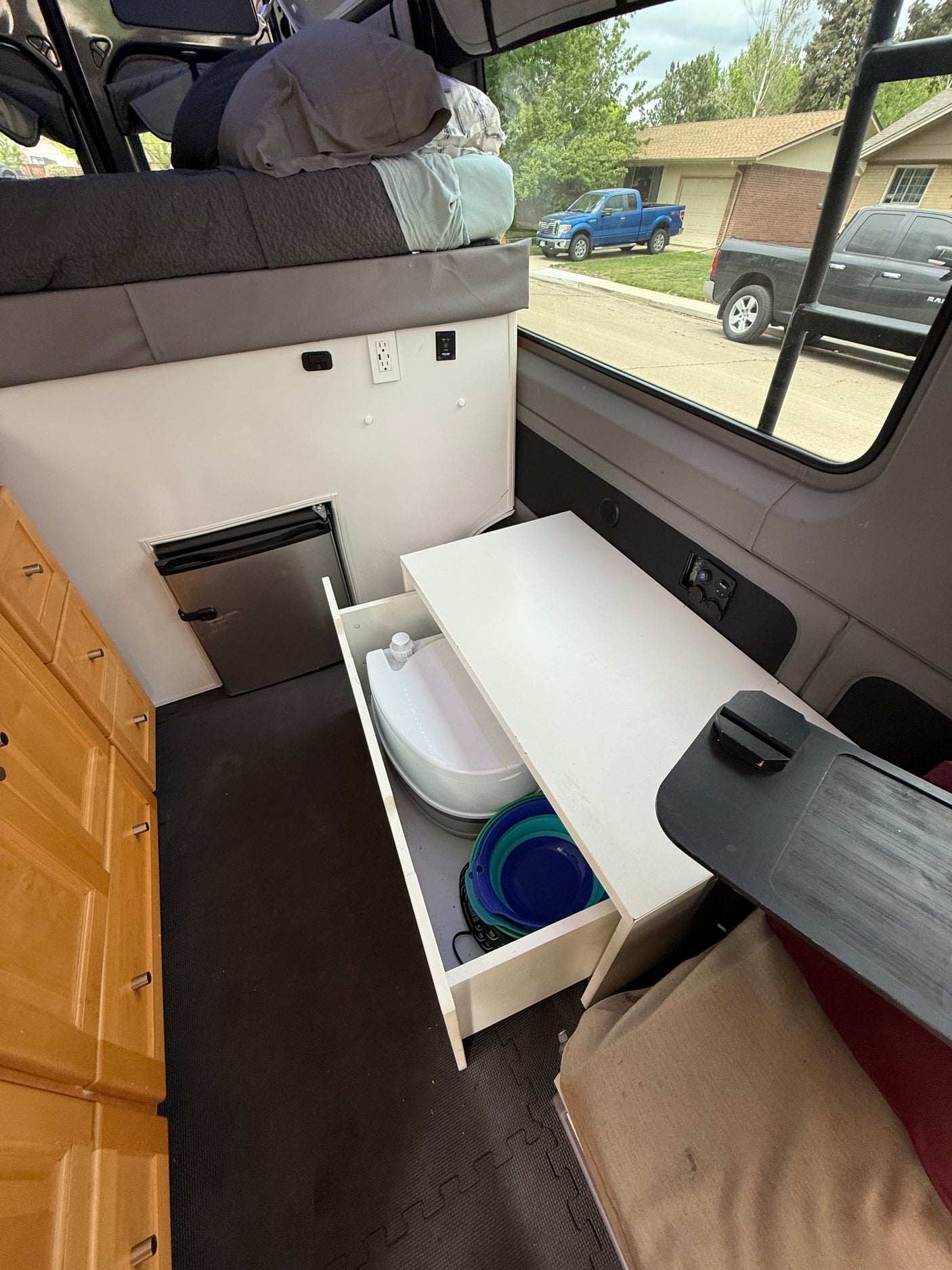 This RV rental camper van showcases a compact interior with an elevated bed, small fridge, pull-out toilet, and cabinets.