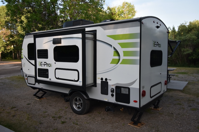 A white Flagstaff E-Pro travel trailer, parked on gravel at a campsite with its slide-out extended, perfect for an RV rental. — photo 8