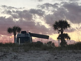 Enjoy a stunning beach sunset from your rv rental! A camper van sits nestled among dunes & palms under a colorful sky.