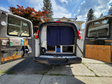 Rear view of a converted van RV rental with open doors, revealing custom storage & blue privacy curtains. Ideal for travel.