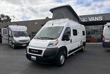 Two white RVs, including a pop-top Ram ProMaster camper van, parked at an rv rental dealership.