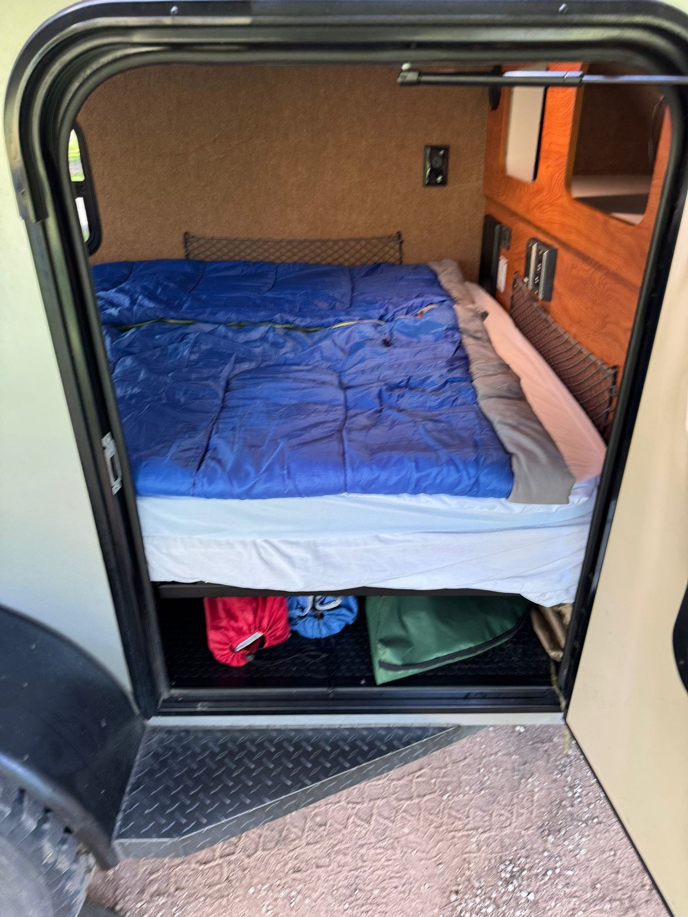 Cozy RV rental interior: bed with blue sleeping bag, wood storage, controls, and textured floor with bags. — photo 5