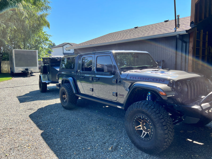 Modified grey Jeep Gladiator towing an off-road camping trailer, with another trailer nearby. Ideal setup for an RV rental adventure!