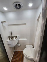 Compact, bright white rv rental bathroom with toilet, small sink, shower curtain, and wooden floor mat.