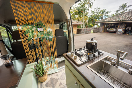 Cozy RV rental interior with kitchenette, sink, and stovetop, offering an outdoor view of a garage and palm trees.
