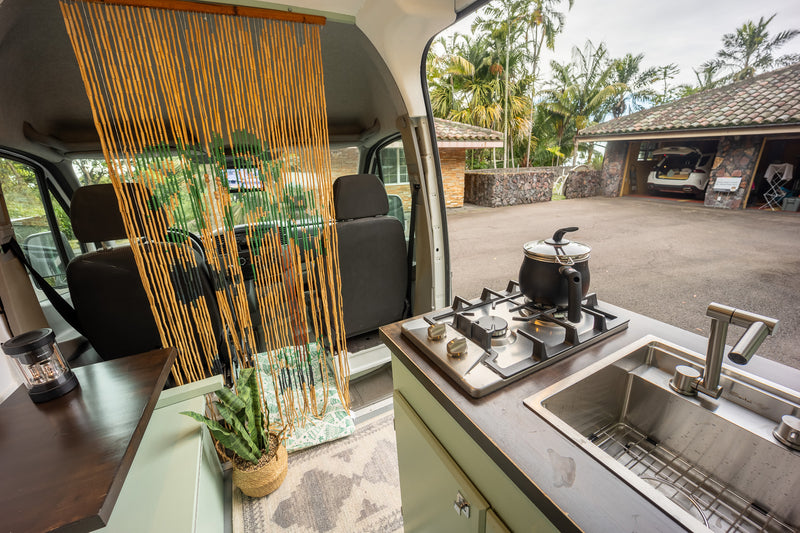 Cozy RV rental interior with kitchenette, sink, and stovetop, offering an outdoor view of a garage and palm trees. — photo 8