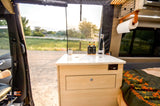 RV rental interior: cozy camper van with a compact kitchen, sink, and an outdoor view. Perfect for a road trip adventure!