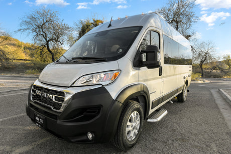 A silver Ram ProMaster camper van RV rental, an Entegra model, parked on asphalt in a sunny desert scene.