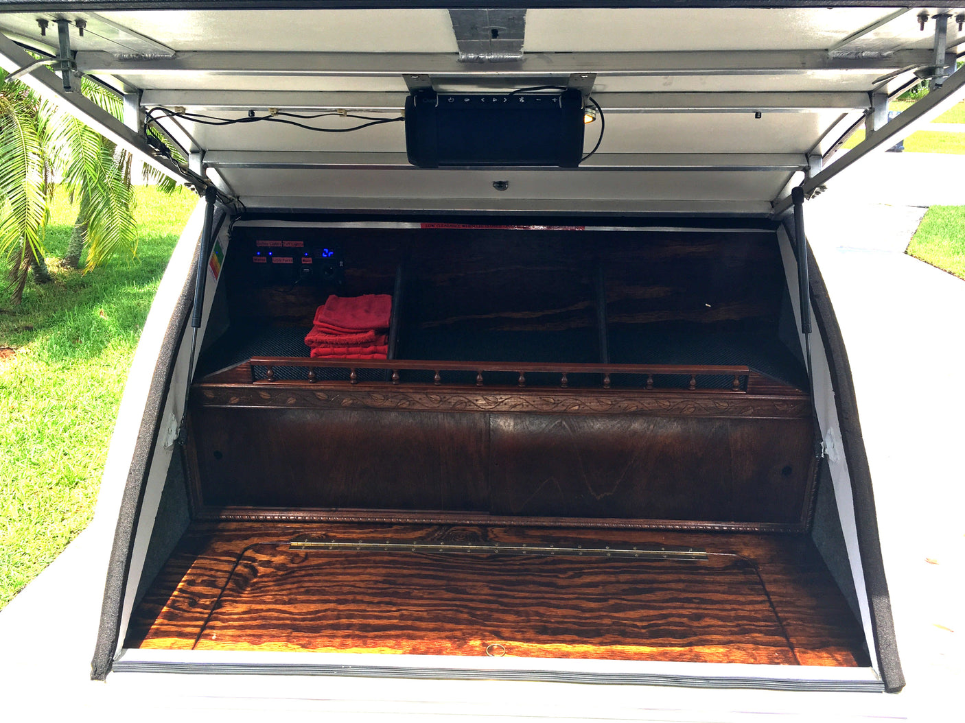 Inside a custom RV rental compartment: a wood interior with a speaker, control panel, and storage space.