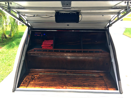 Inside a custom RV rental compartment: a wood interior with a speaker, control panel, and storage space.