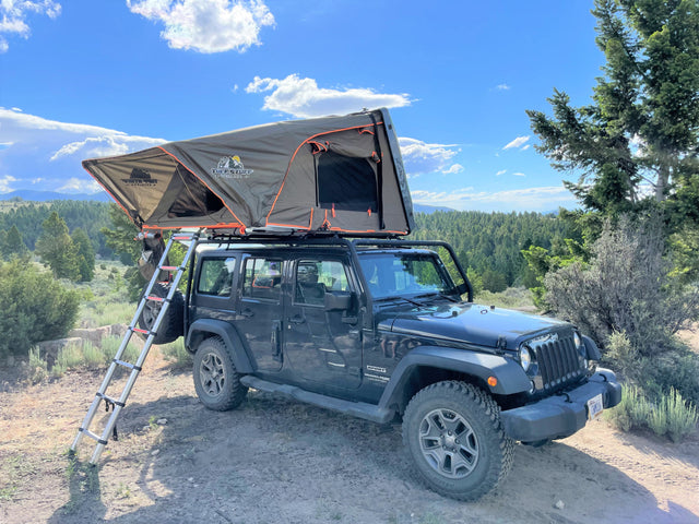 Black Jeep Wrangler with an open Tuff Stuff rooftop tent and ladder, an ideal RV rental for off-grid camping adventures.