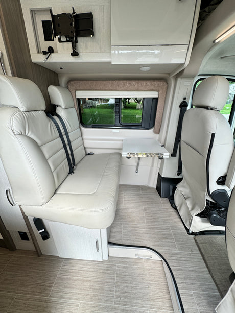 Bright RV rental interior features comfy bench seating, a practical fold-down table, and a wall-mounted entertainment setup.
