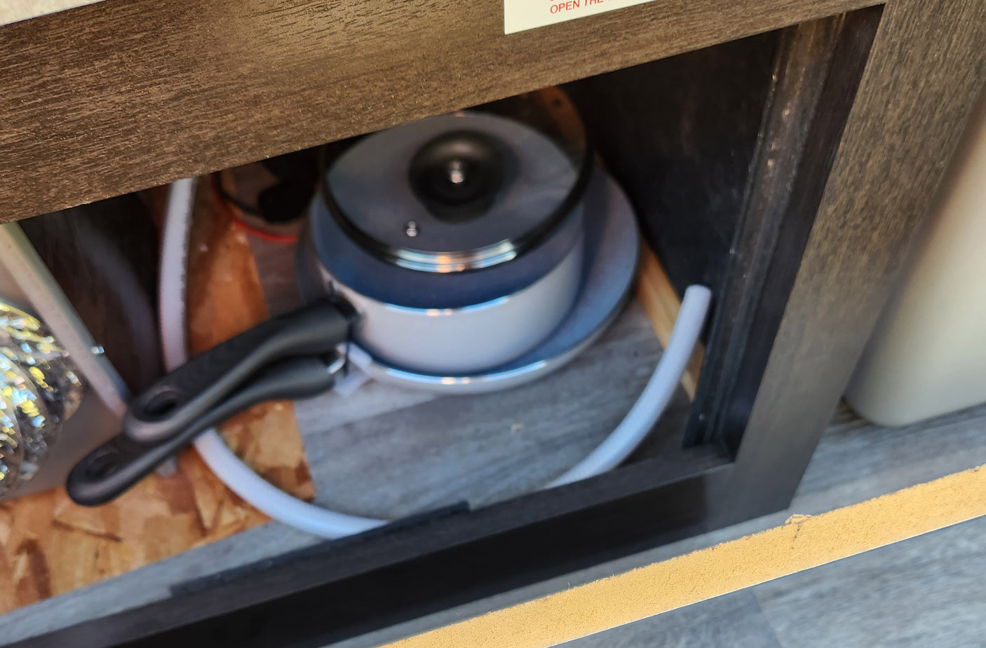 Inside an RV rental cabinet: a stacked cooking pot with lid, a plate, and a coiled white hose, ready for use.